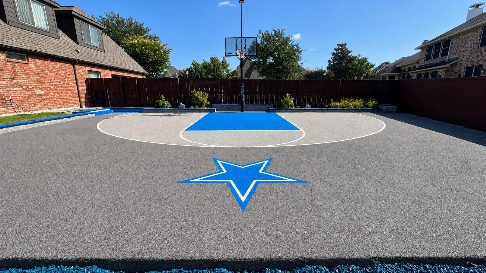Residential basketball half court with blue key, star logo, and in-ground hoop