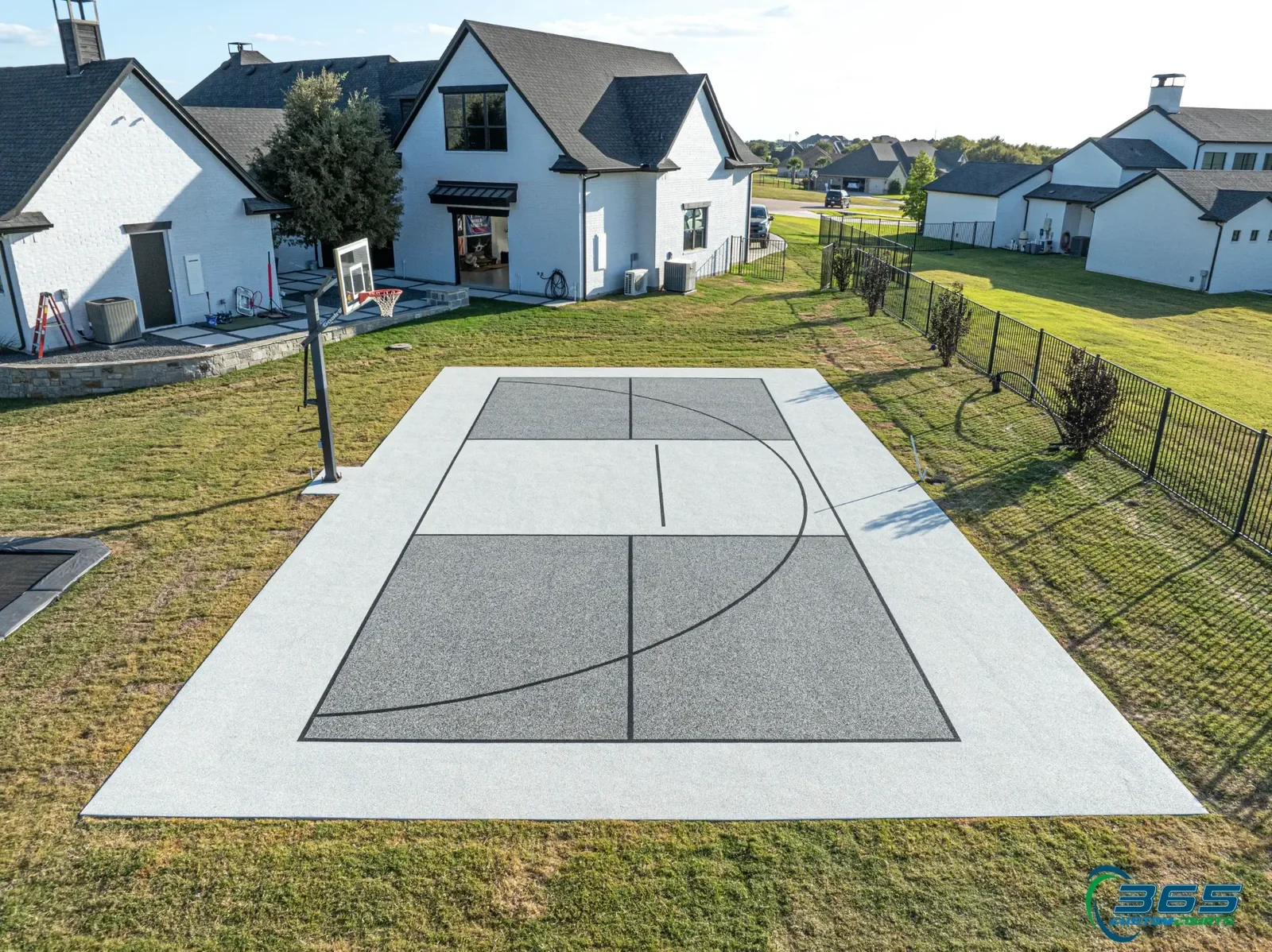 Gray two-tone backyard basketball half court behind a white brick home
