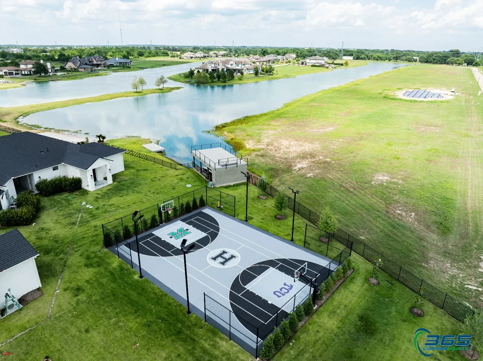 Lighted full backyard basketball court with custom logos beside a lake