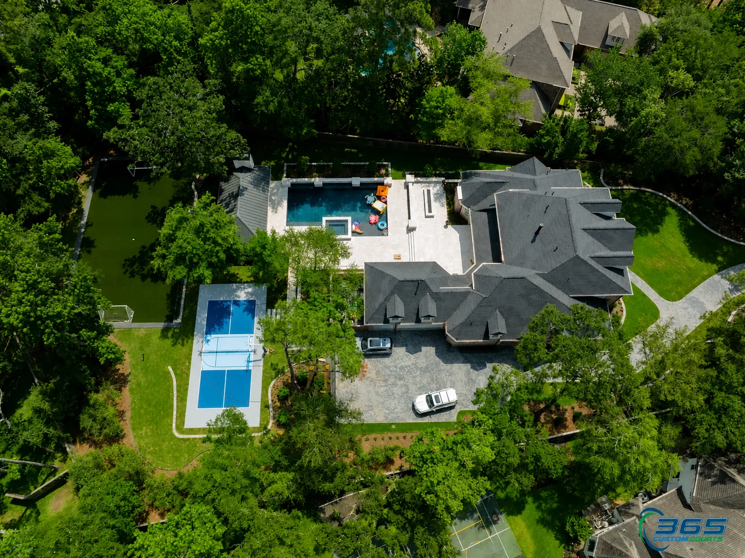 High aerial view of a wooded estate with a compact blue pickleball court and pool