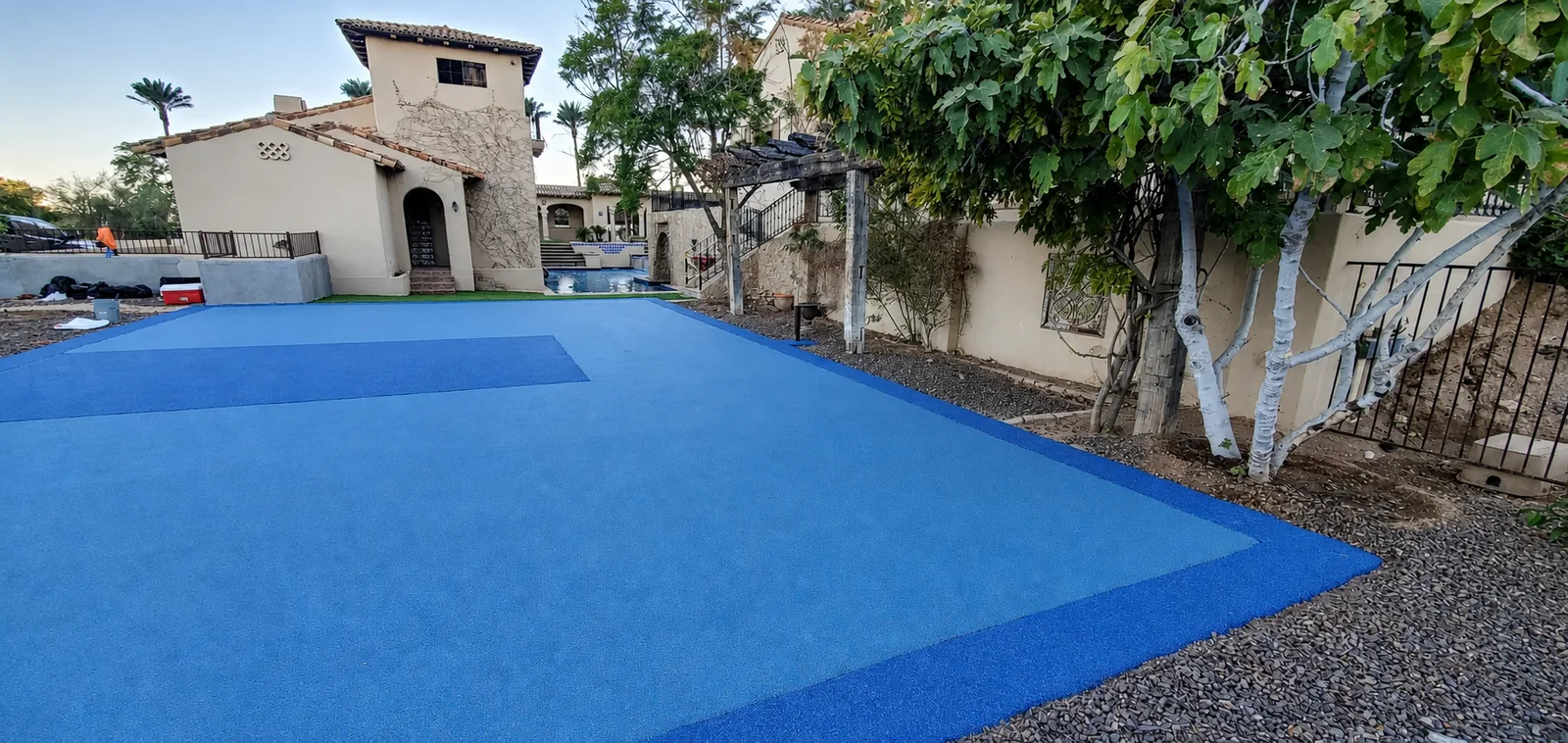 Blue residential multi-sport surface beside a Spanish-style estate