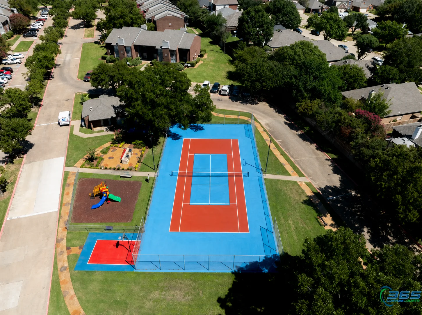 Aerial view of a community tennis court, basketball area, and playground