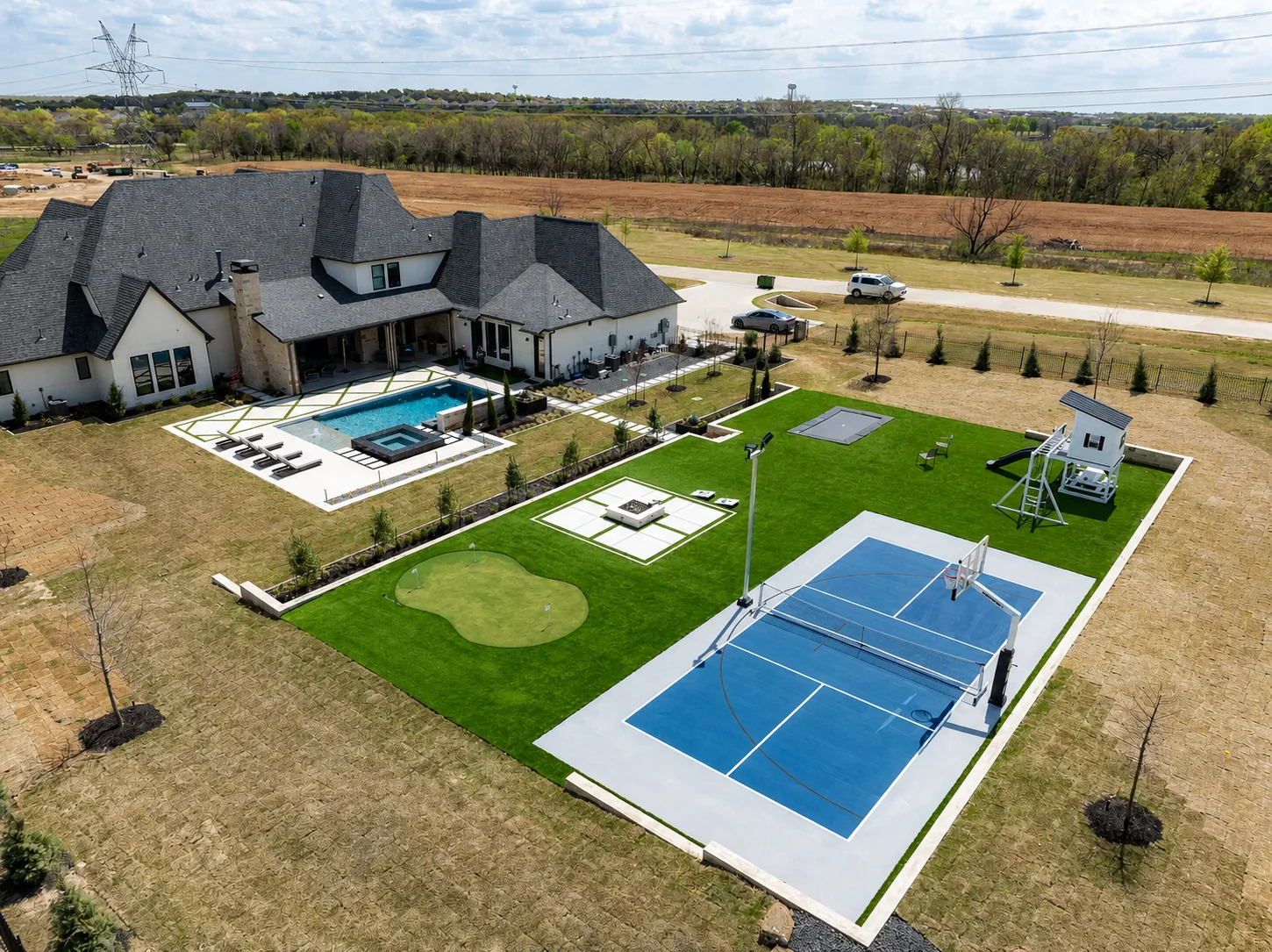 Aerial view of an estate with a blue multi-sport court, basketball equipment, a pool, and a putting green